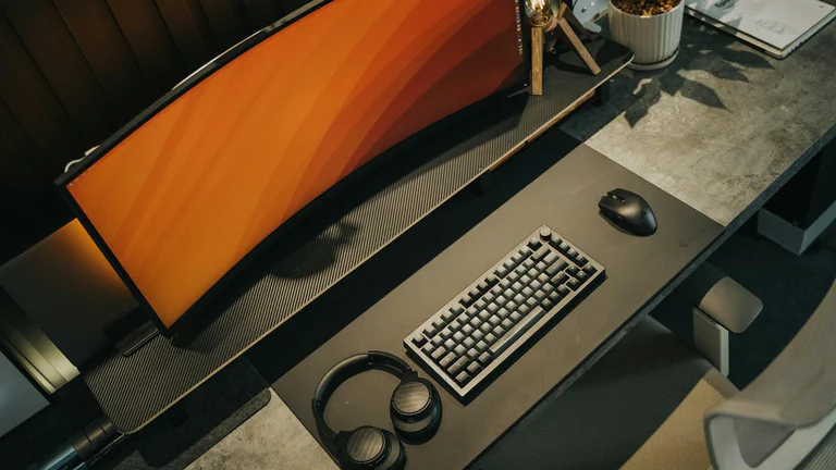 Ultrawide-Gaming-Monitor mit mechanischer Tastatur, Maus und Kopfhörern auf einem aufgeräumten Schreibtisch.