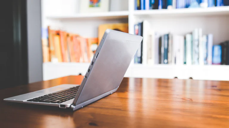 A laptop open on a wooden desk with bookshelves in the background, used as a student laptop buying guide cover.