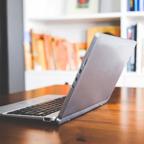 A laptop open on a wooden desk with bookshelves in the background, used as a student laptop buying guide cover.