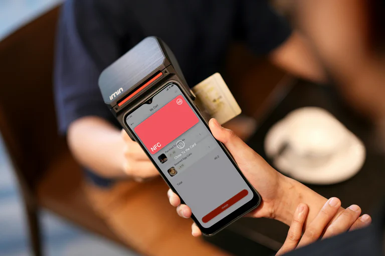 A smartphone held near a payment terminal during an NFC contactless payment.